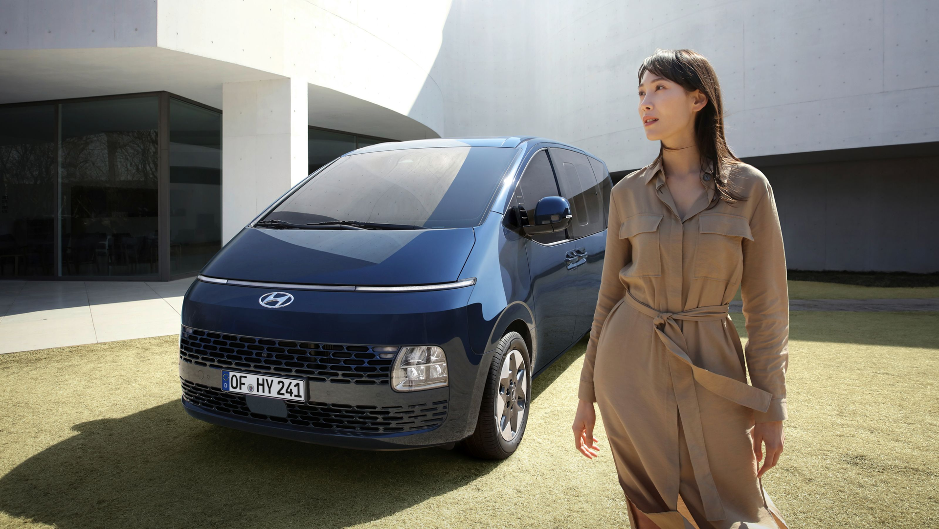 A woman is standing in front of a blue van. Staria
