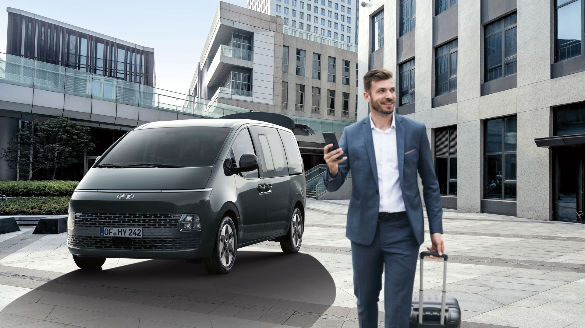 A man in a suit is walking towards a van while holding a suitcase and a cell  Stariaphone.
