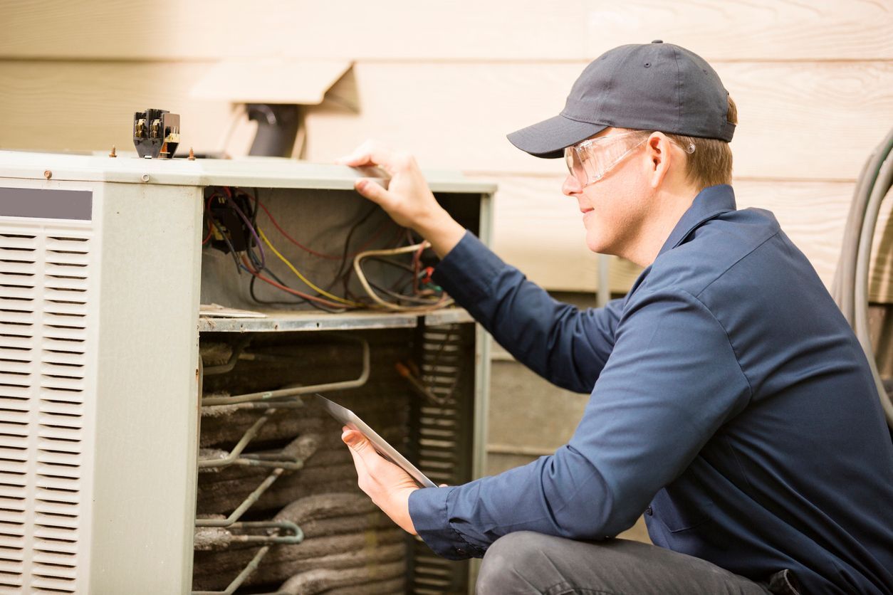 A man is working on an air conditioner while looking at a tablet.
