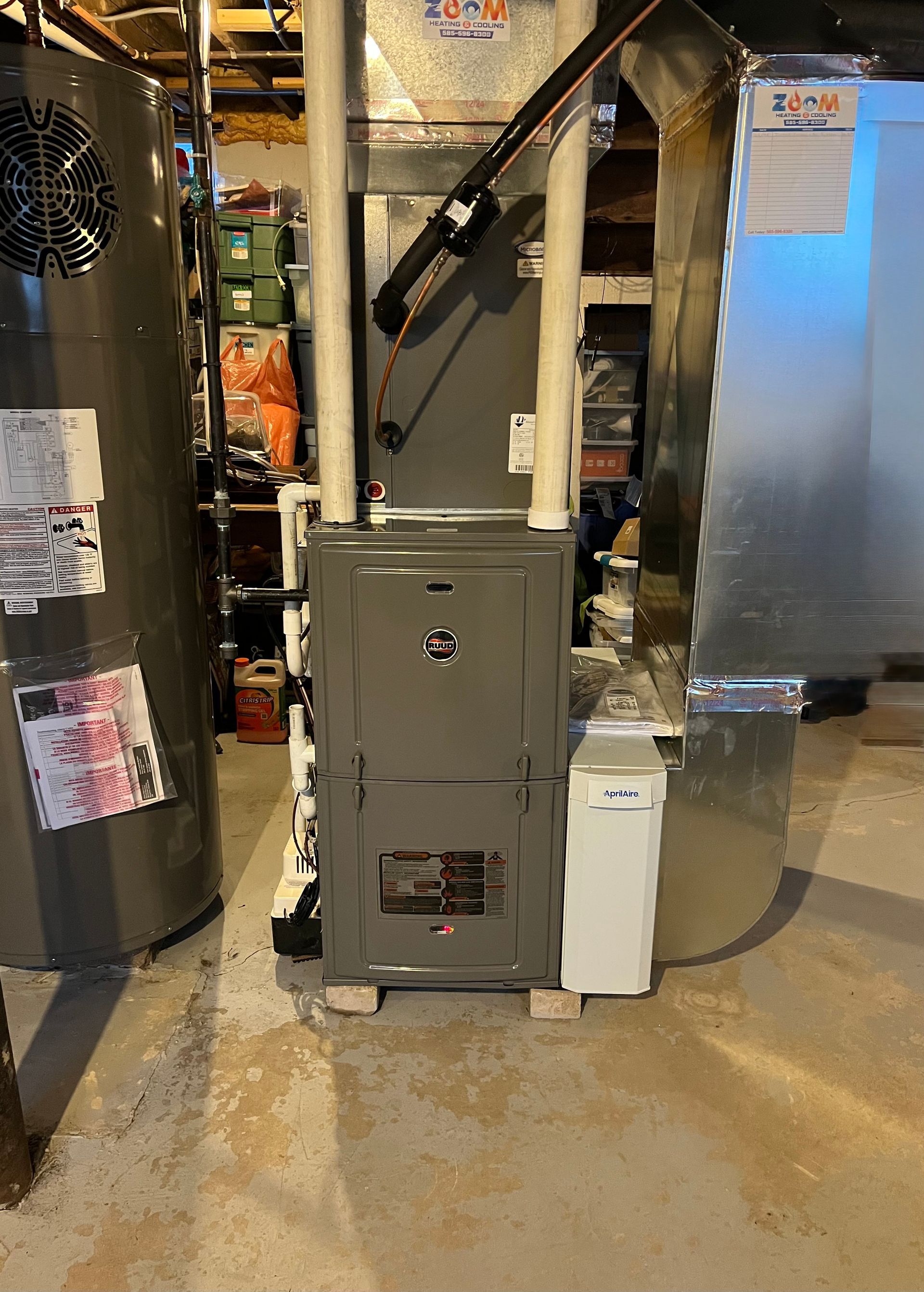 A gray furnace is sitting next to a white pipe