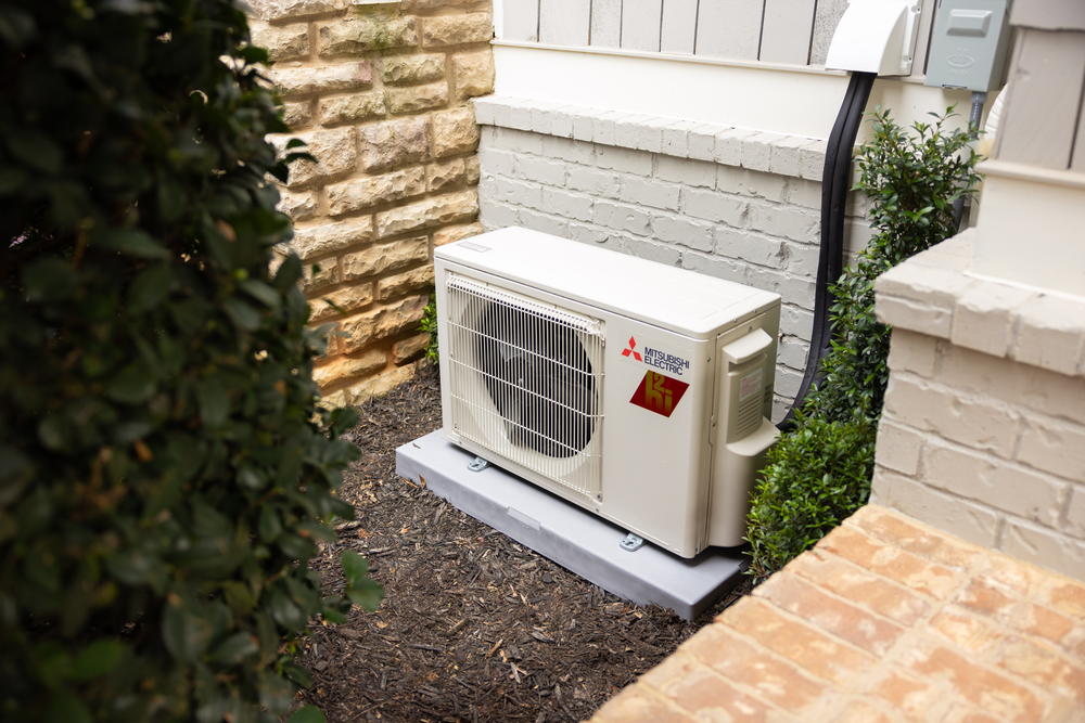 A white air conditioner is sitting on top of a concrete platform next to a brick wall.
