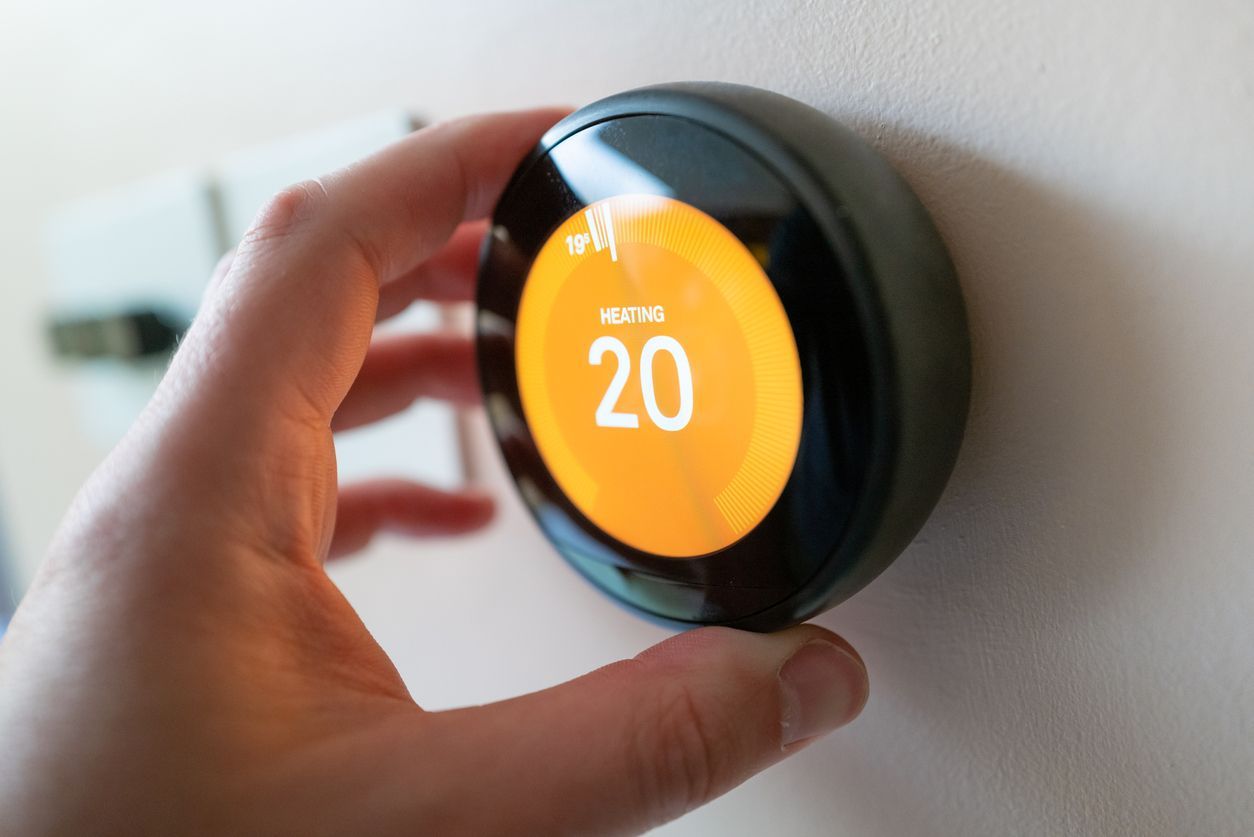 A person is adjusting a smart thermostat on a wall.