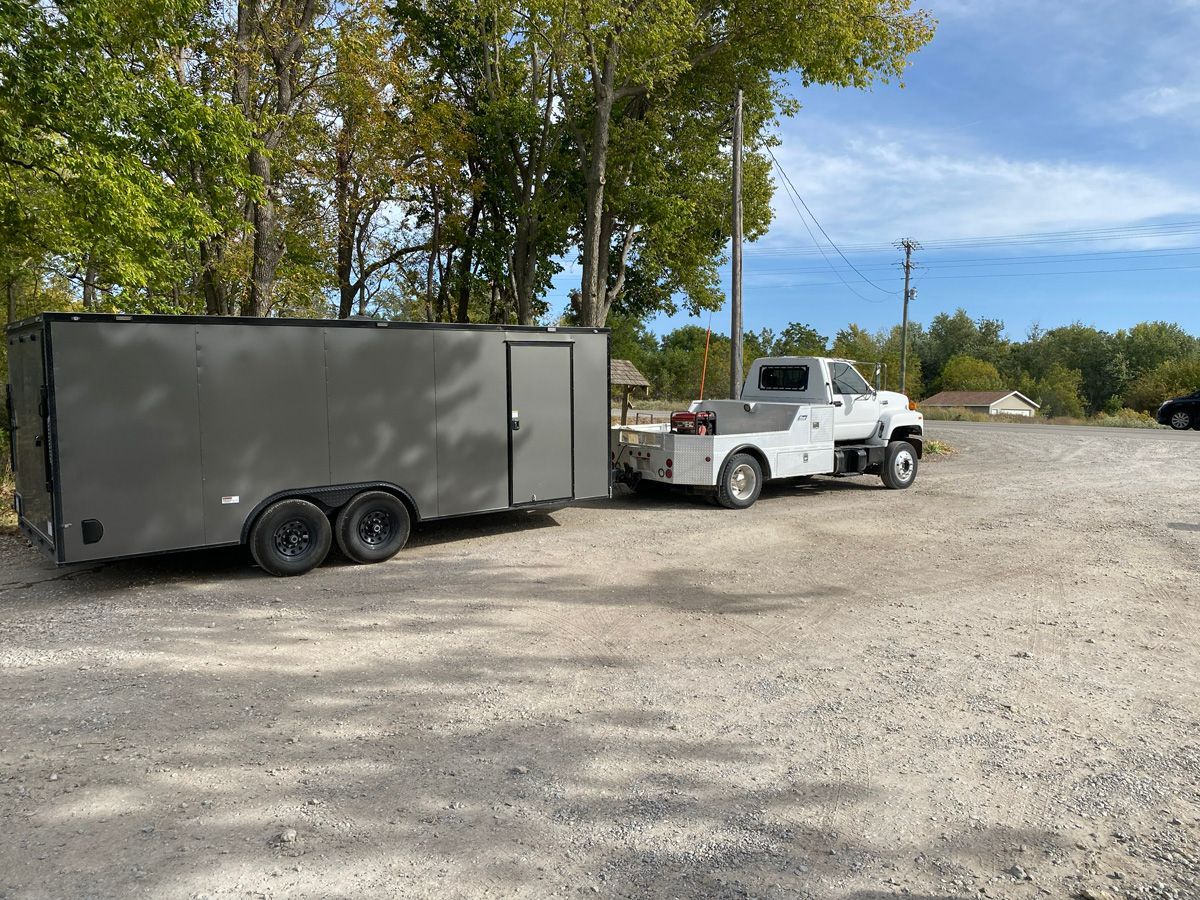 A trailer is being towed by a white truck in a gravel lot.