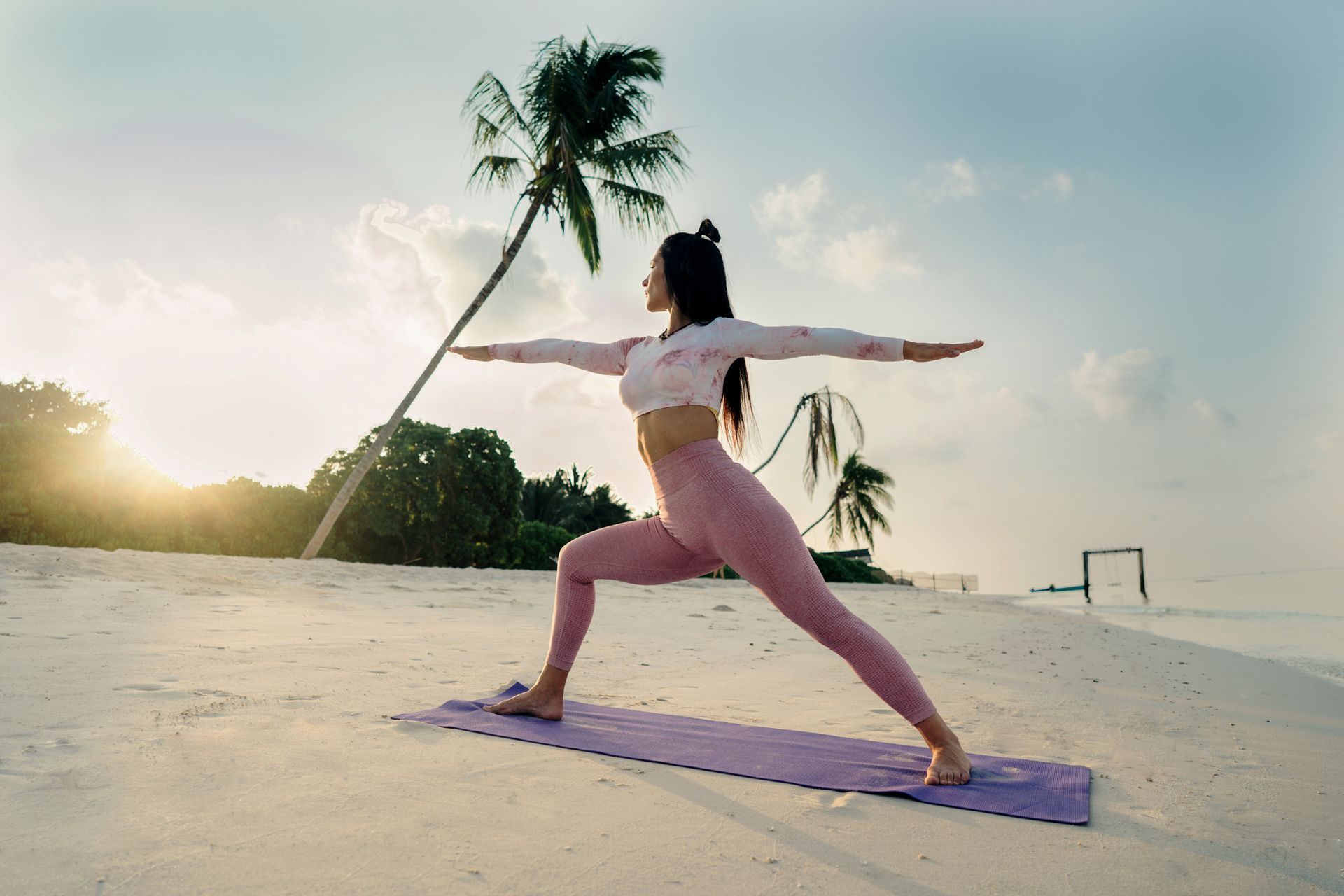 A woman is practicing yoga on the beach at sunset.