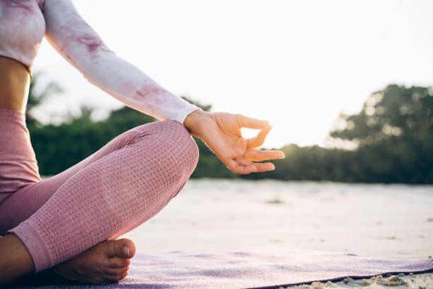 A woman is sitting on a yoga mat on the beach.