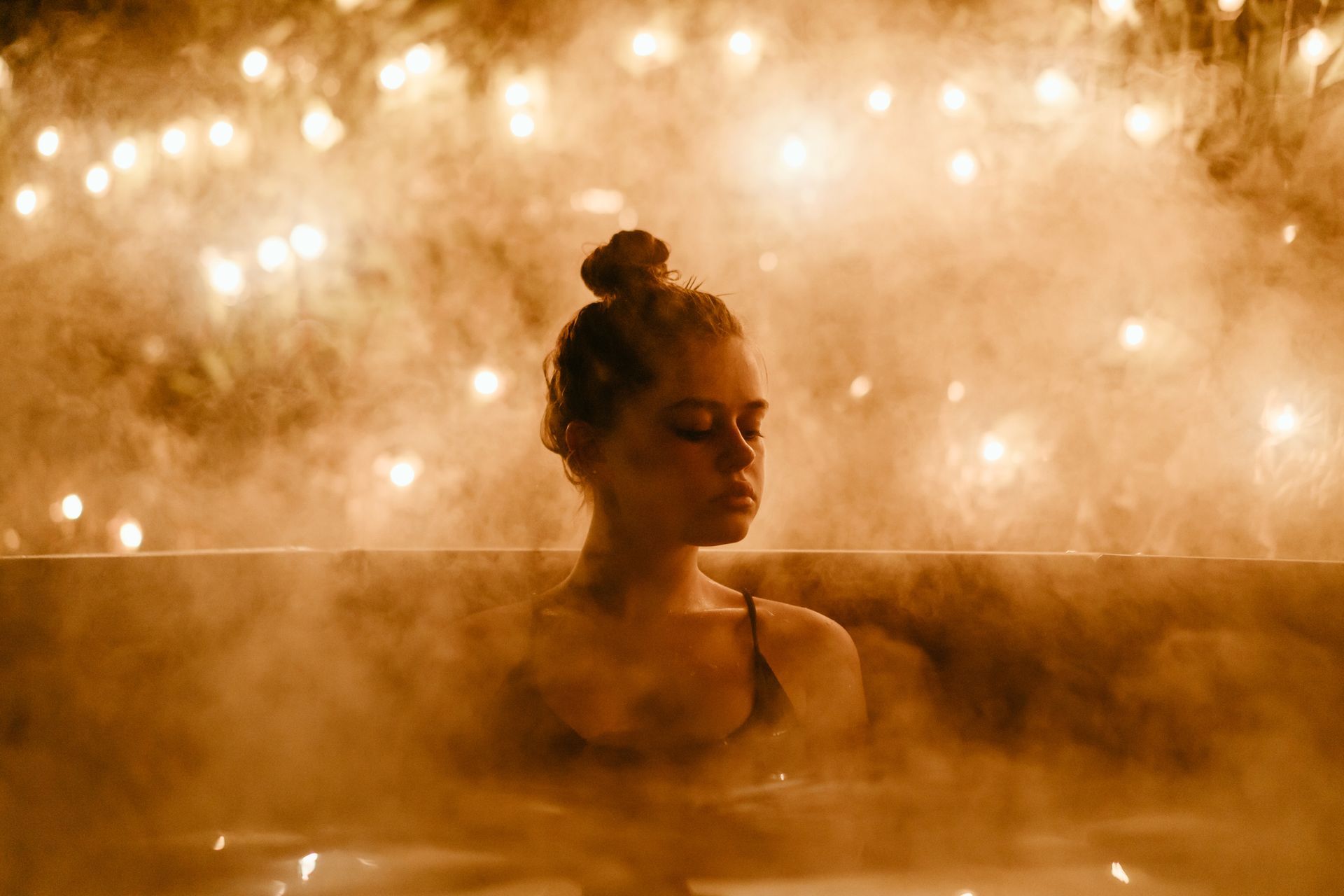 A woman is taking a bath in a hot tub surrounded by lights.