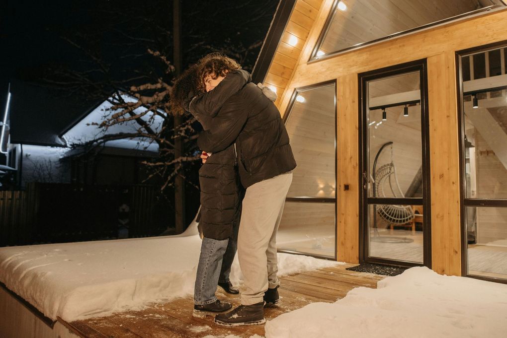 Two people embracing in front of a cabin on a snowy night.
