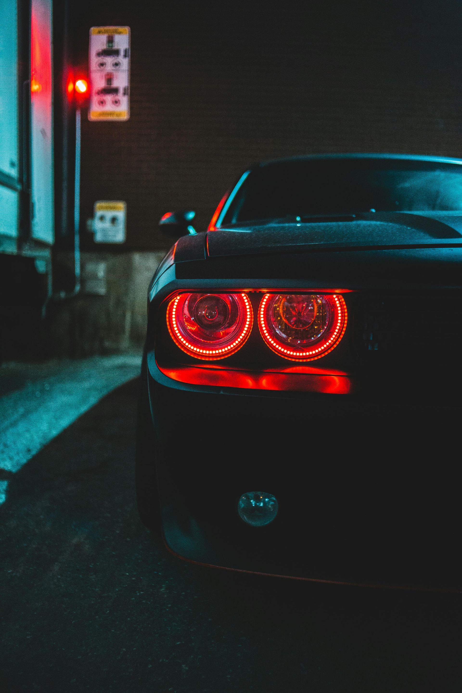 A black car with red lights is parked in a parking lot at night.