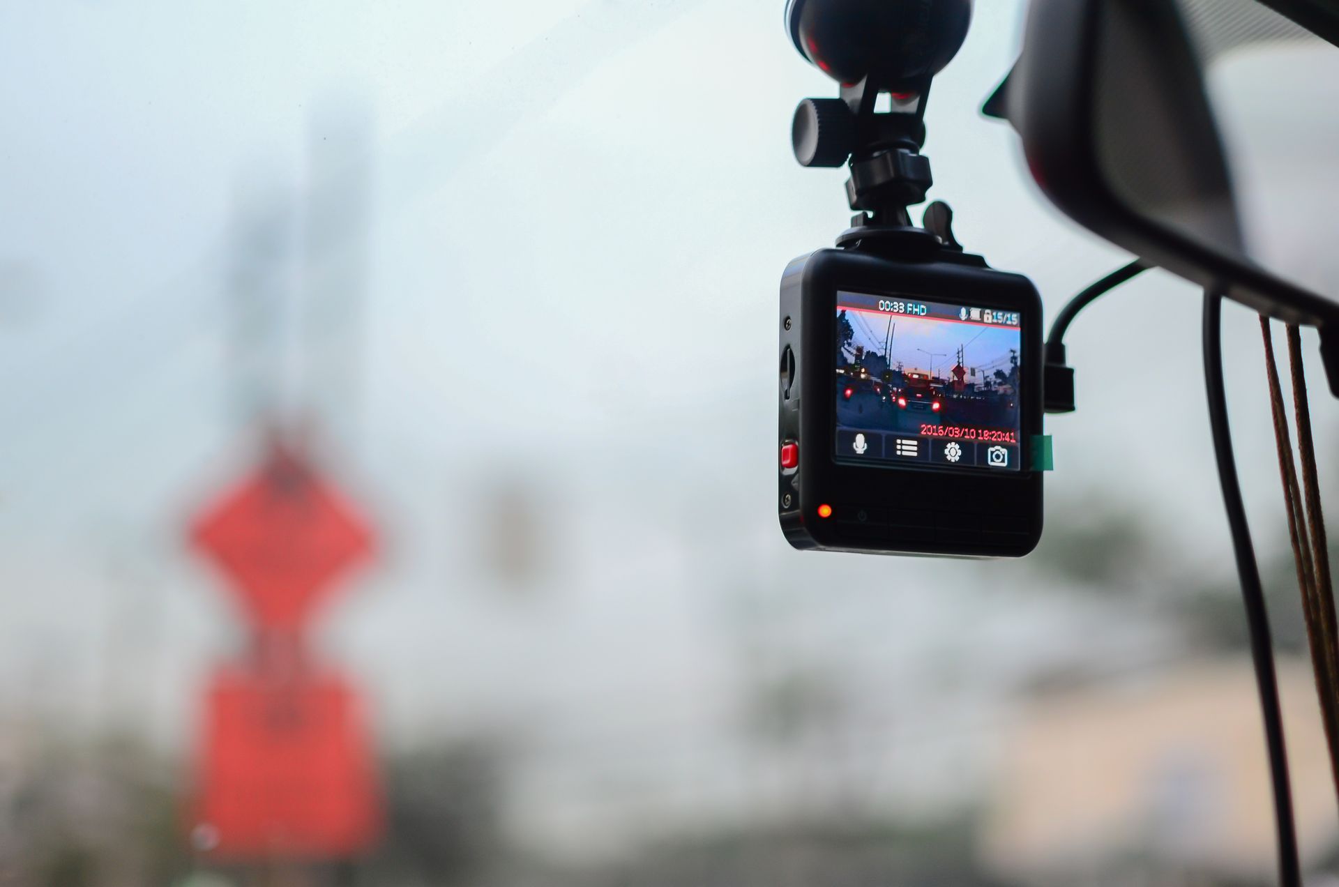 A dash cam is hanging from the rear view mirror of a car.