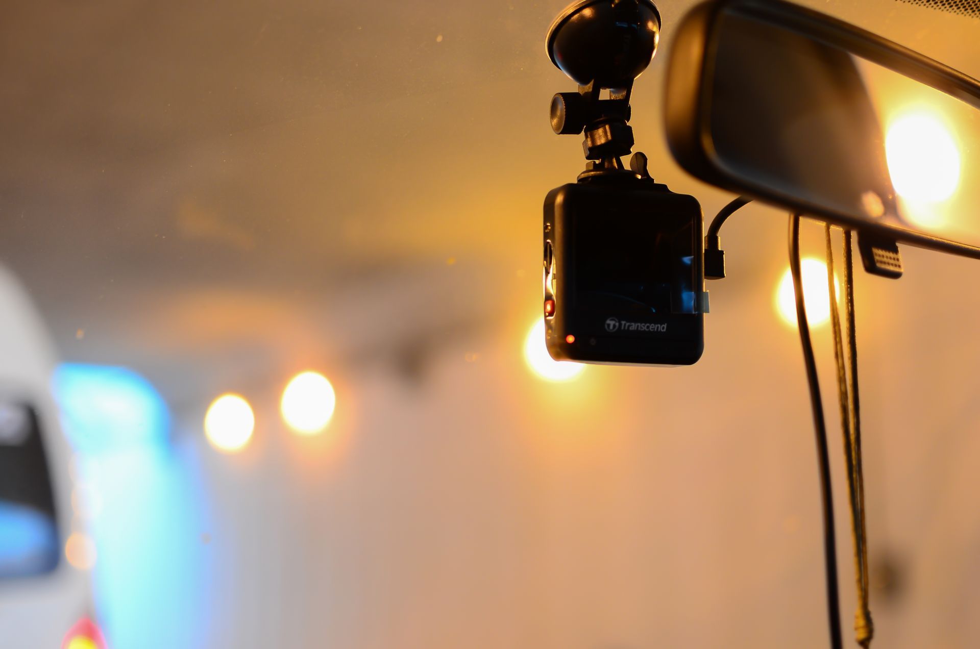 A dash cam is hanging from the rear view mirror of a car.