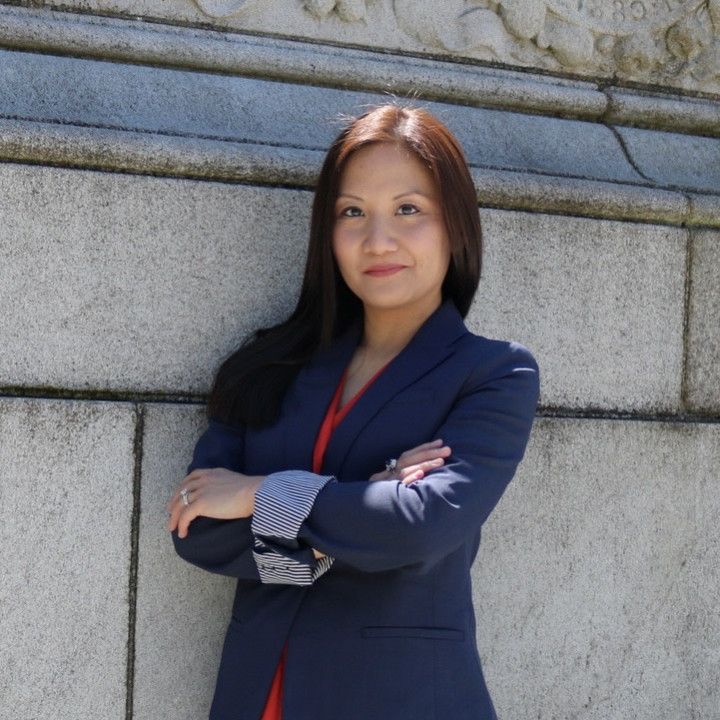 Woman in a blue blazer with arms crossed, smiling in front of a stone wall.