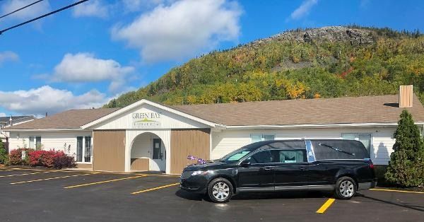 Black SUV parked in front of a small beige building with mountains and blue sky behind it
