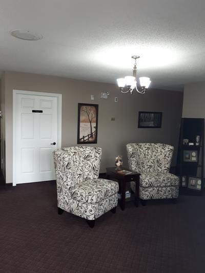 Empty living room with two patterned armchairs, small table, chandelier, and white door on beige walls.