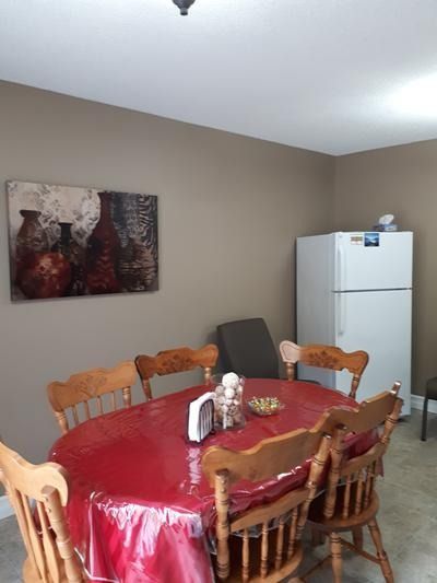 Dining area with a round red table, wooden chairs, wall art, and a white refrigerator.