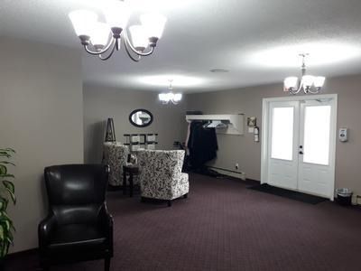 Empty lobby with purple carpet, black chair, chandelier lights, and double glass doors.