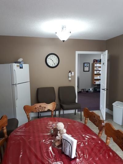 Dining room with a red tablecloth, wooden chairs, a white fridge, and an open doorway to another room.