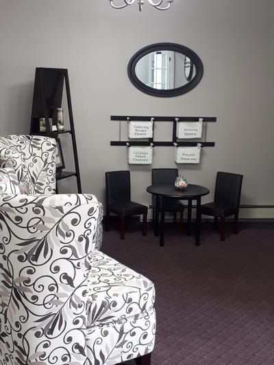 Sitting area with patterned chairs, small table, wall mirror, and framed signs in a quiet lobby.