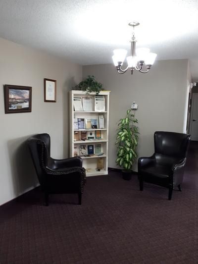 Small waiting room with two black chairs, a white shelf, potted plant, and overhead light.