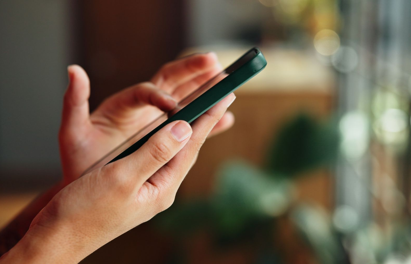 Hands holding a smartphone indoors, with a blurred warm background