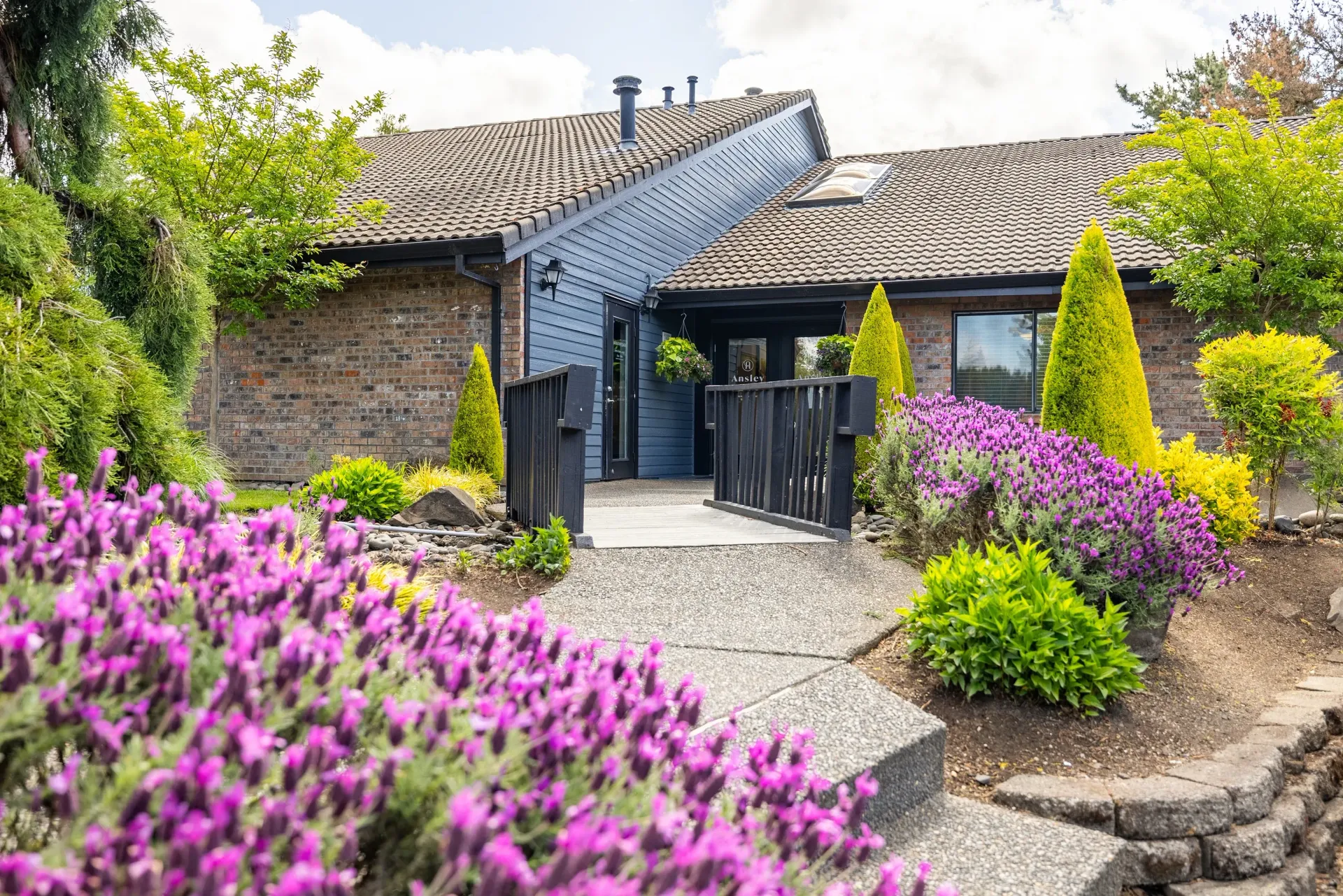 Stone building with purple flowers, walkway, and landscaping.
