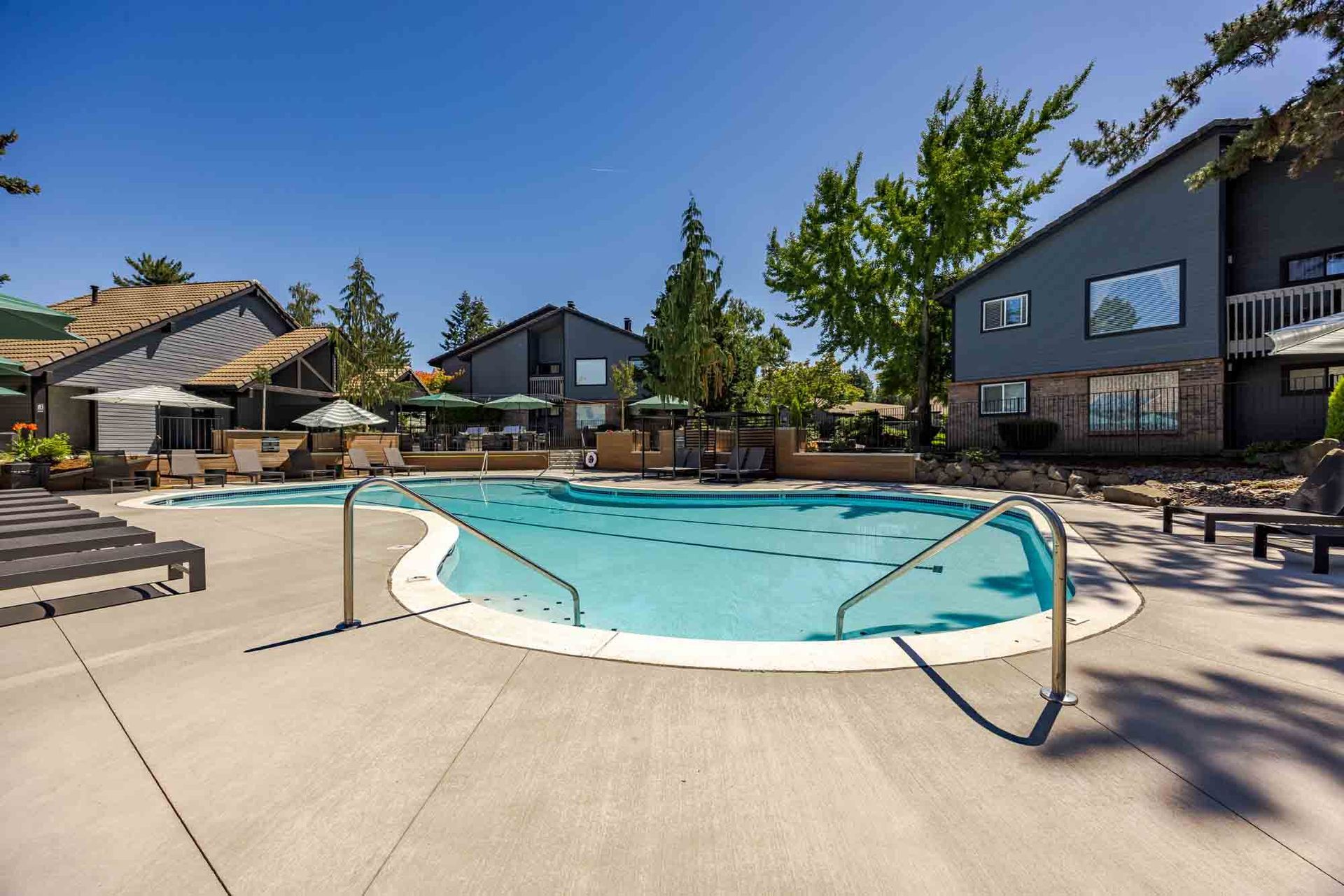 Swimming pool with clear water and lounge chairs; a brick building in the background.