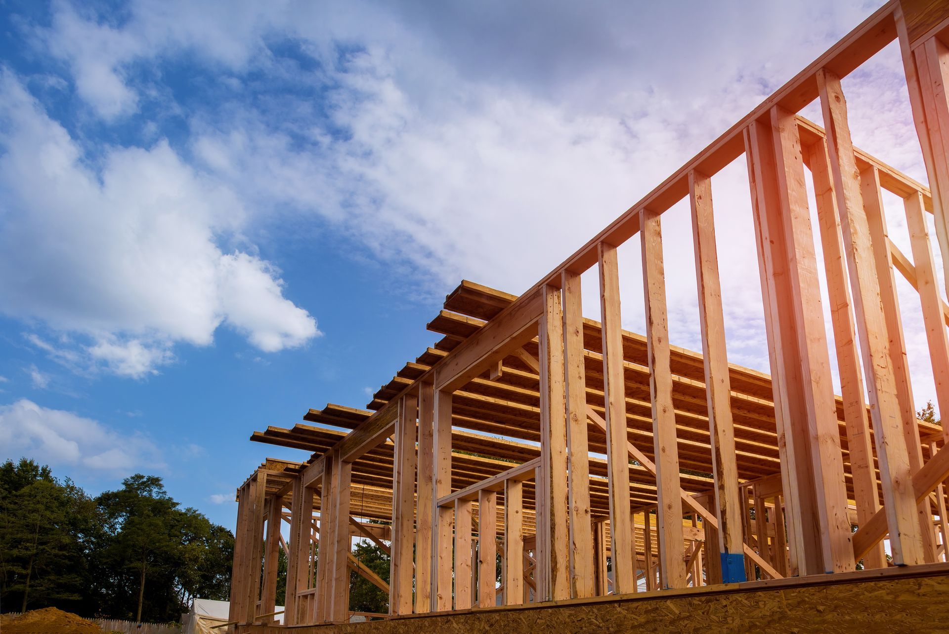 Wooden frame of a house under construction against a blue sky with clouds.