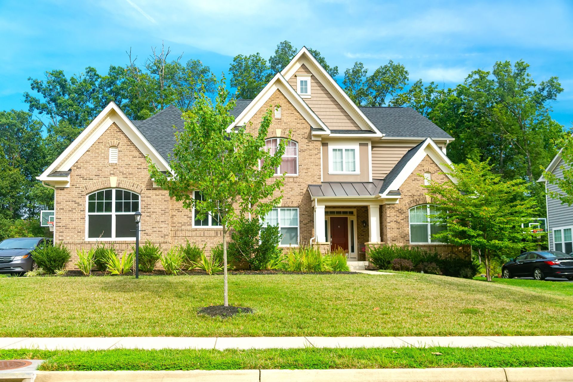 Two-story brick house with a green lawn and trees under a bright blue sky. Two-story brick house with a green lawn and trees under a bright blue sky.