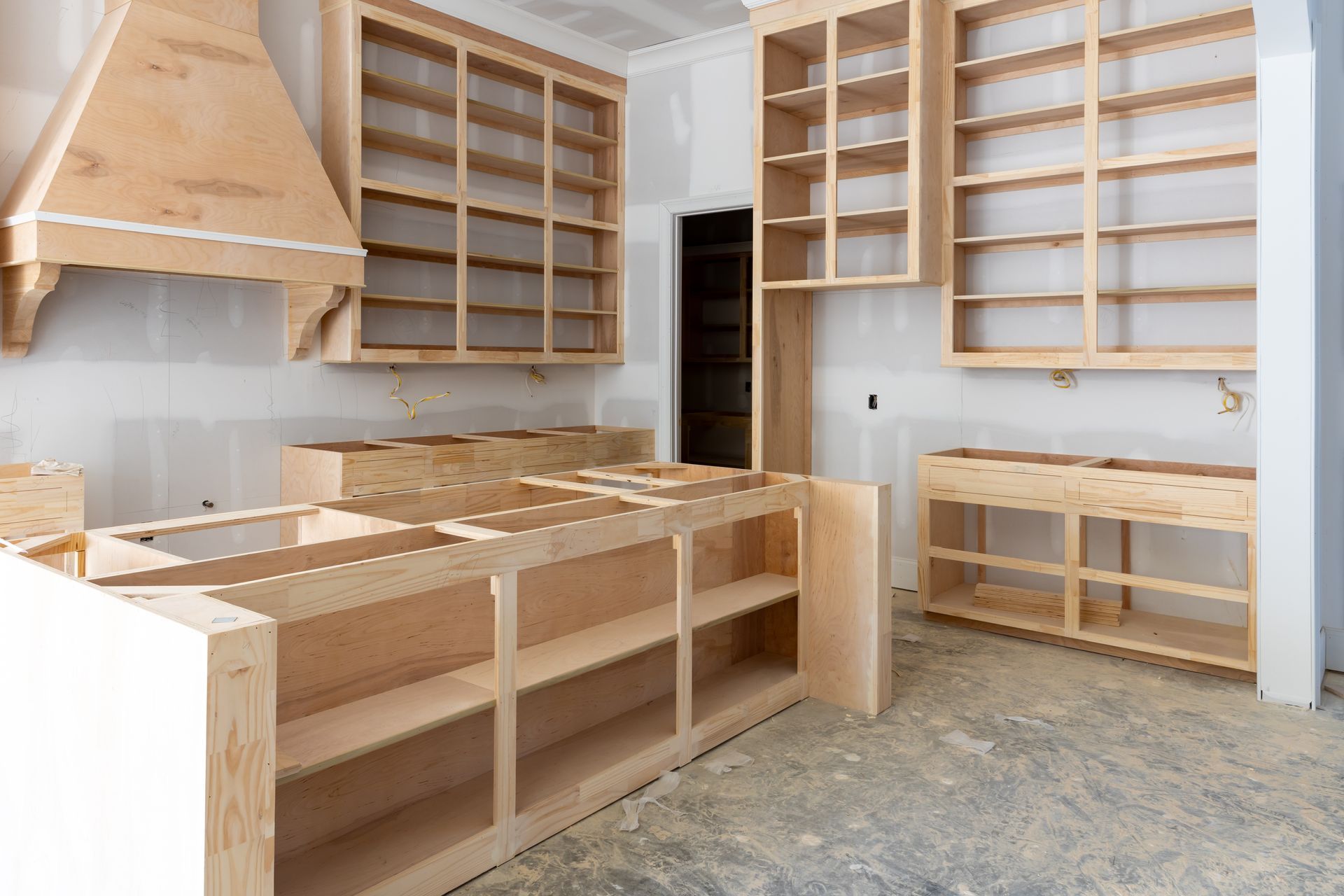 Unfinished kitchen cabinetry installation: island, upper and lower cabinets, range hood.