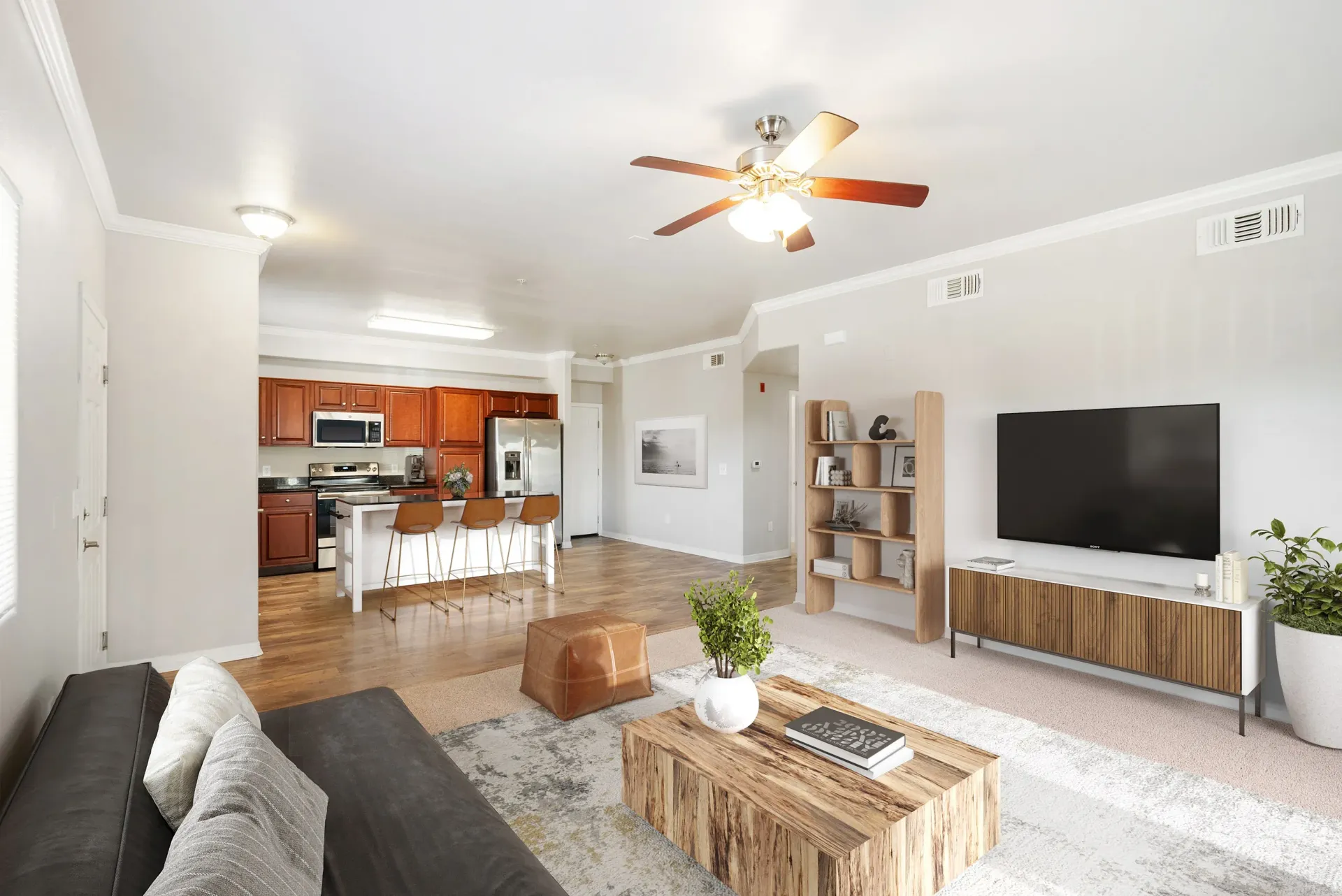 Open-concept living room and kitchen with sofa, TV, and a bar-height island with stools at Wolf Ranch Apartments.