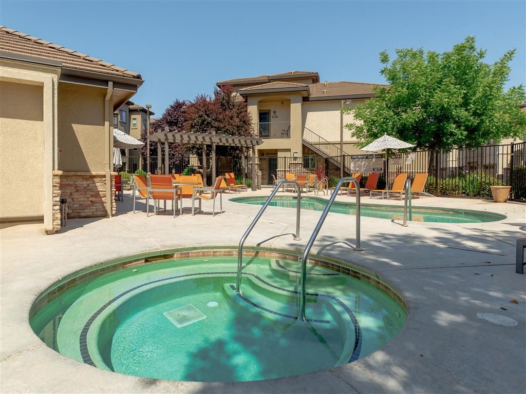 Outdoor pool and hot tub area with orange lounge chairs and umbrellas at Wolf Ranch Apartments.
