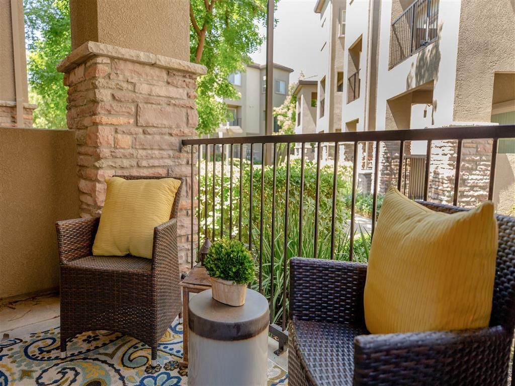 Balcony seating area with two wicker chairs, yellow cushions, and a small table on an apartment terrace at Wolf Ranch Apartments.