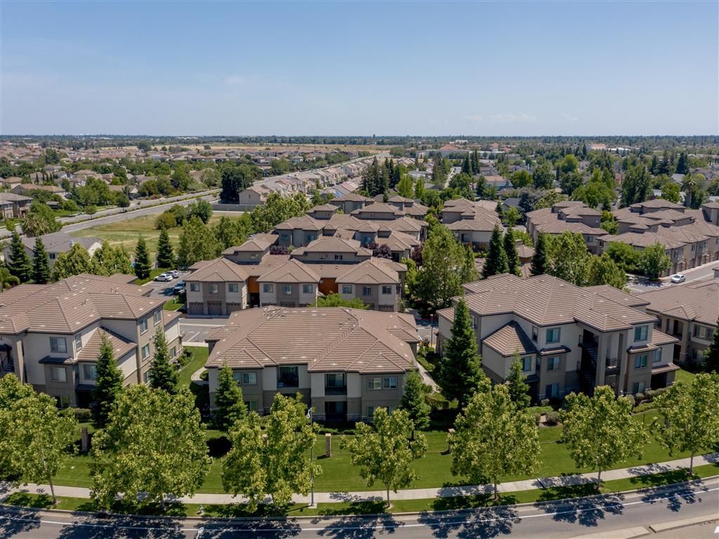 Aerial view of a beige apartment community with clustered buildings, green lawns, and tree-lined streets at Wolf Ranch Apartments.