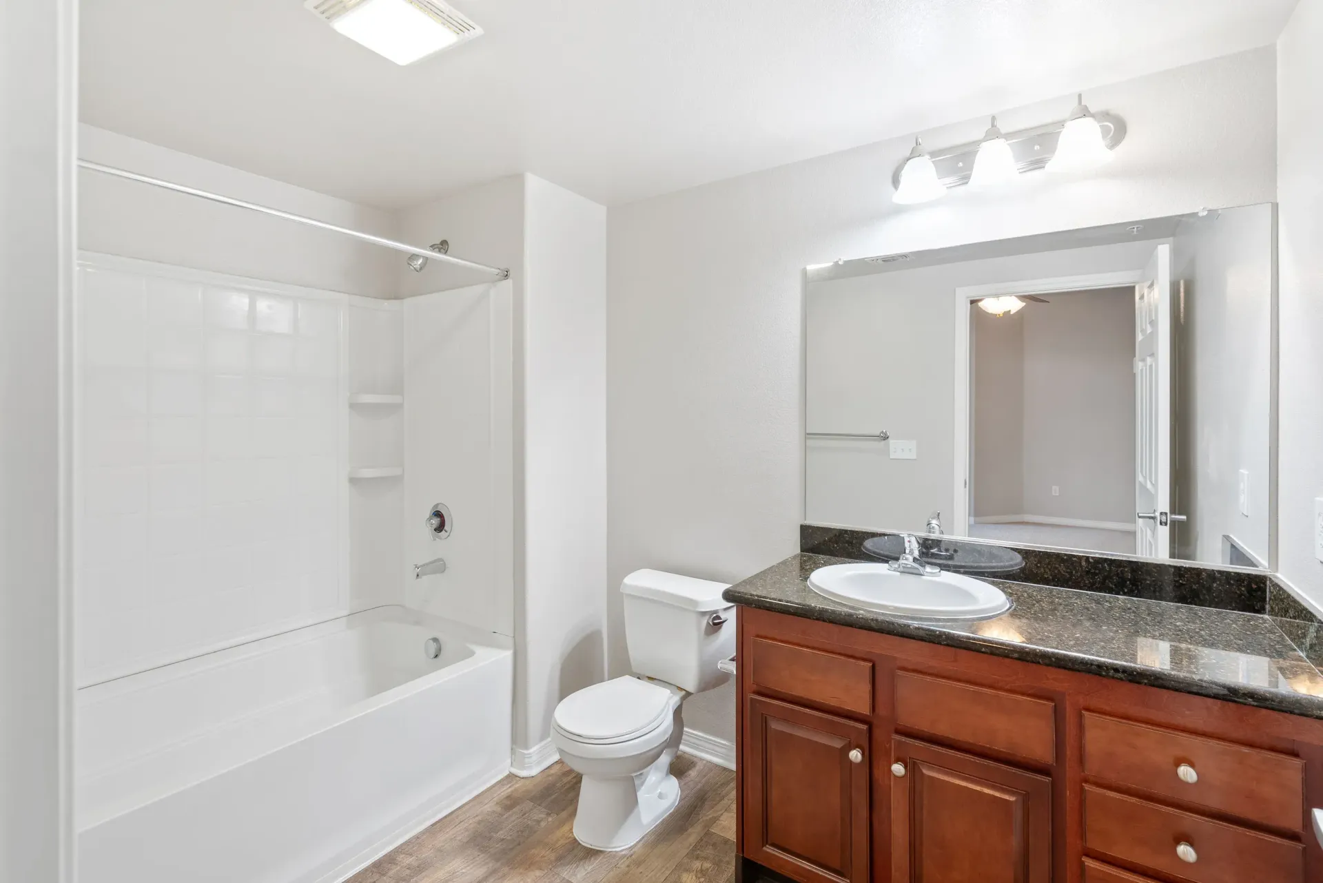Bathroom with white-tiled tub/shower, toilet, and dark granite vanity at Wolf Ranch Apartments.