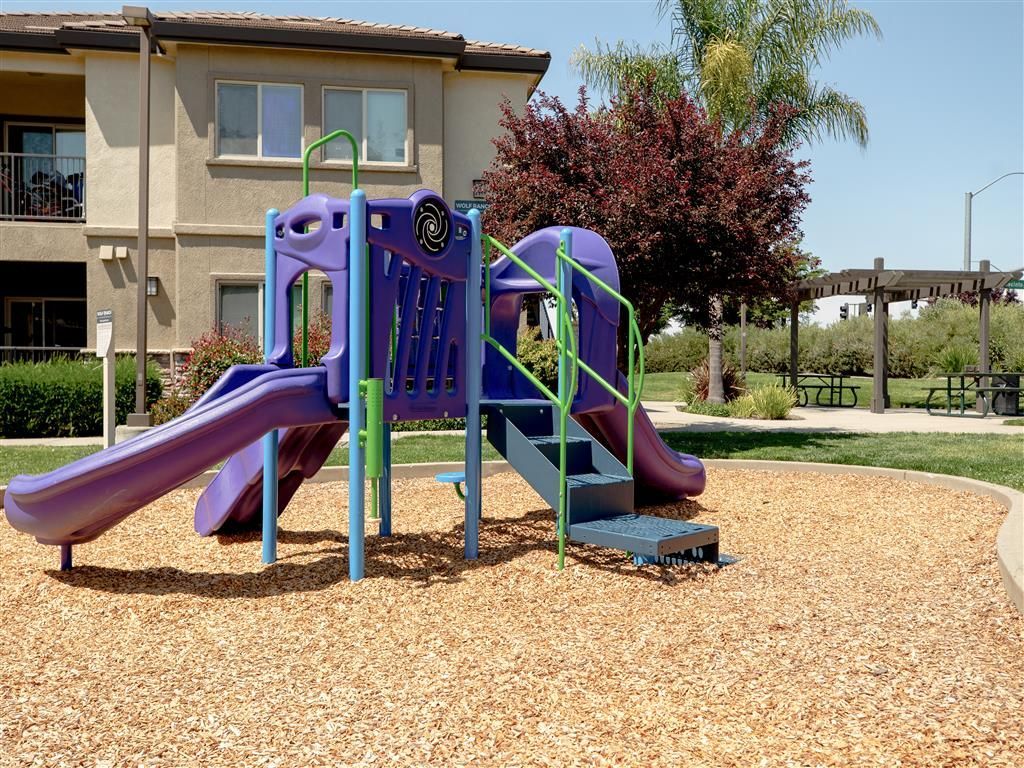 Outdoor playground with purple slides and green rails in a residential courtyard at Wolf Ranch Apartments.