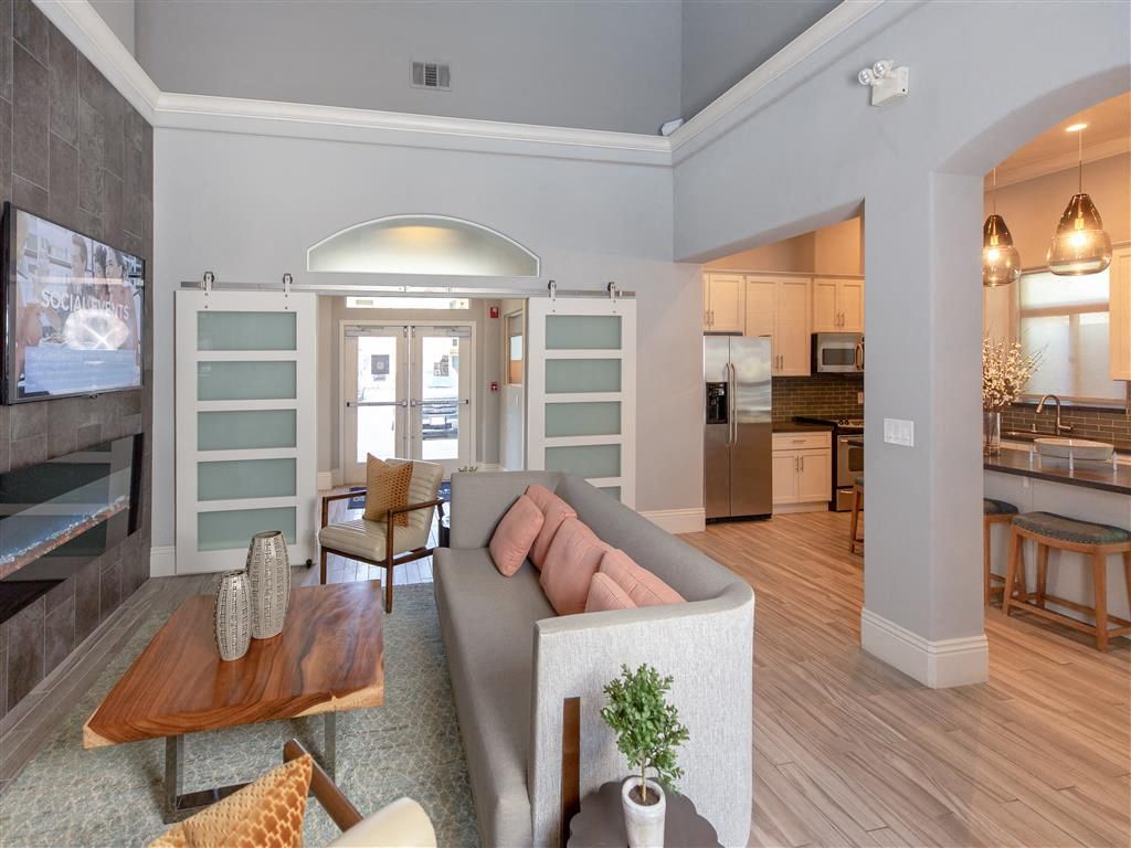 Open-concept lounge with a gray sofa, coffee table, and adjacent kitchen in a clubhouse at Wolf Ranch Apartments.