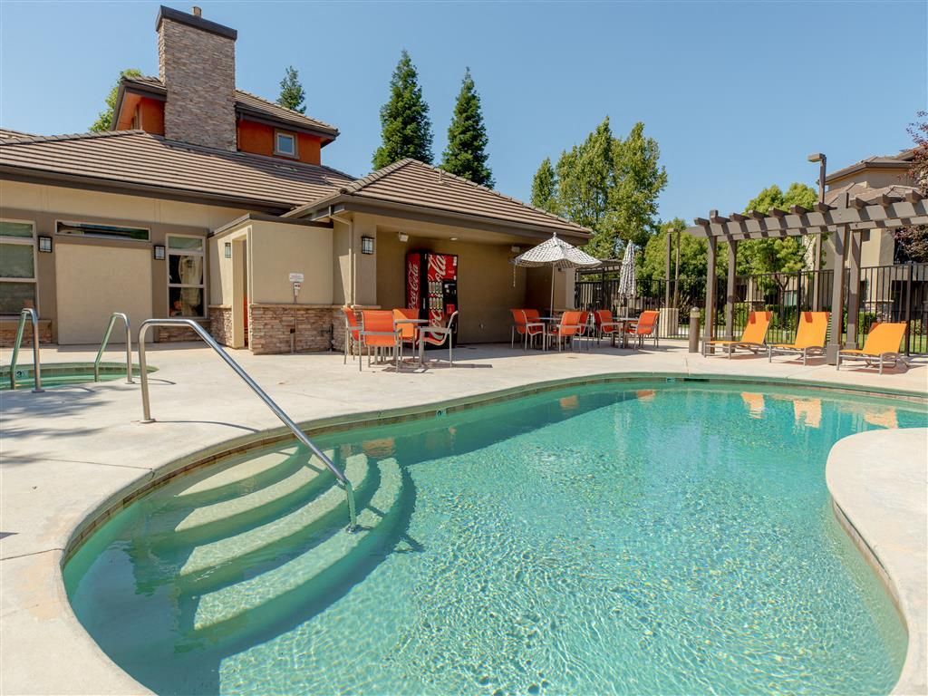 Outdoor pool at an apartment community with lounge chairs, umbrellas, and a shaded patio at Wolf Ranch Apartments.