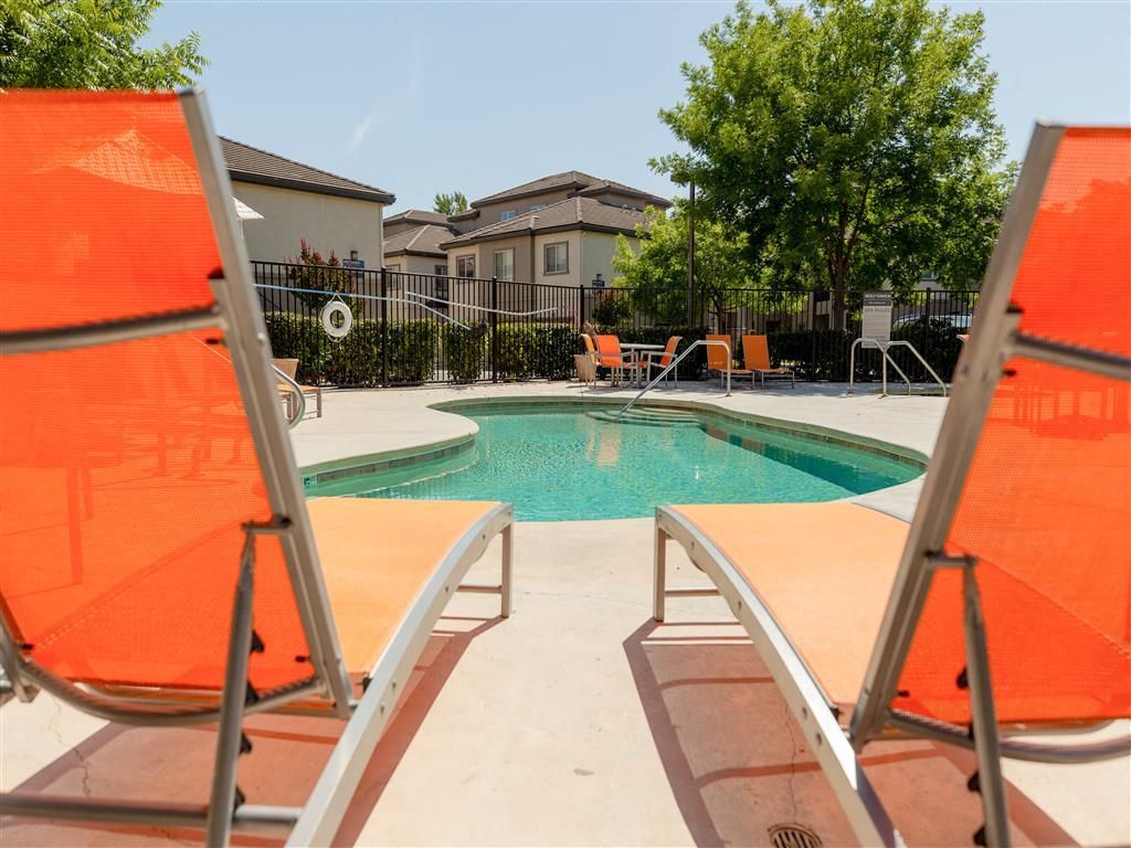 Outdoor apartment pool with orange lounge chairs and surrounding fence at Wolf Ranch Apartments.