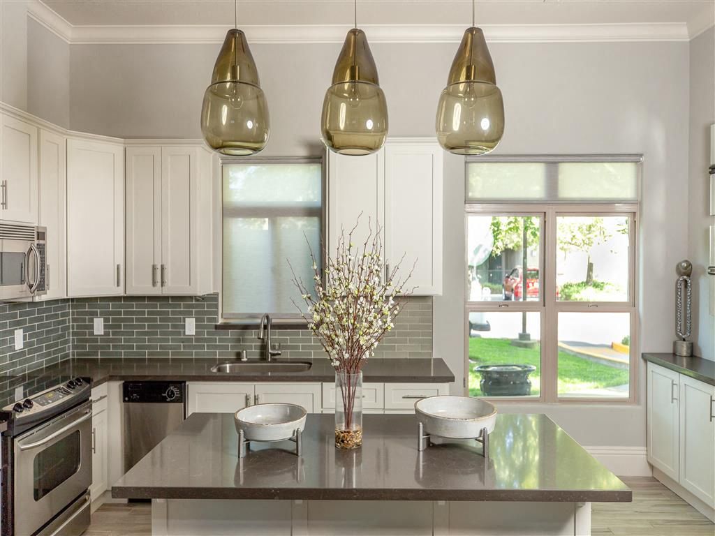 Modern kitchen with white cabinets, gray countertops, island, pendant lights, and window at Wolf Ranch Apartments.