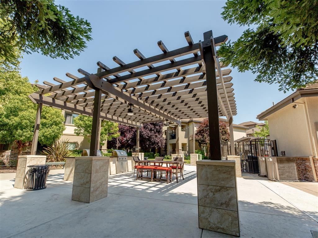 Outdoor community space with a large pergola, seating, and grills at Wolf Ranch Apartments.