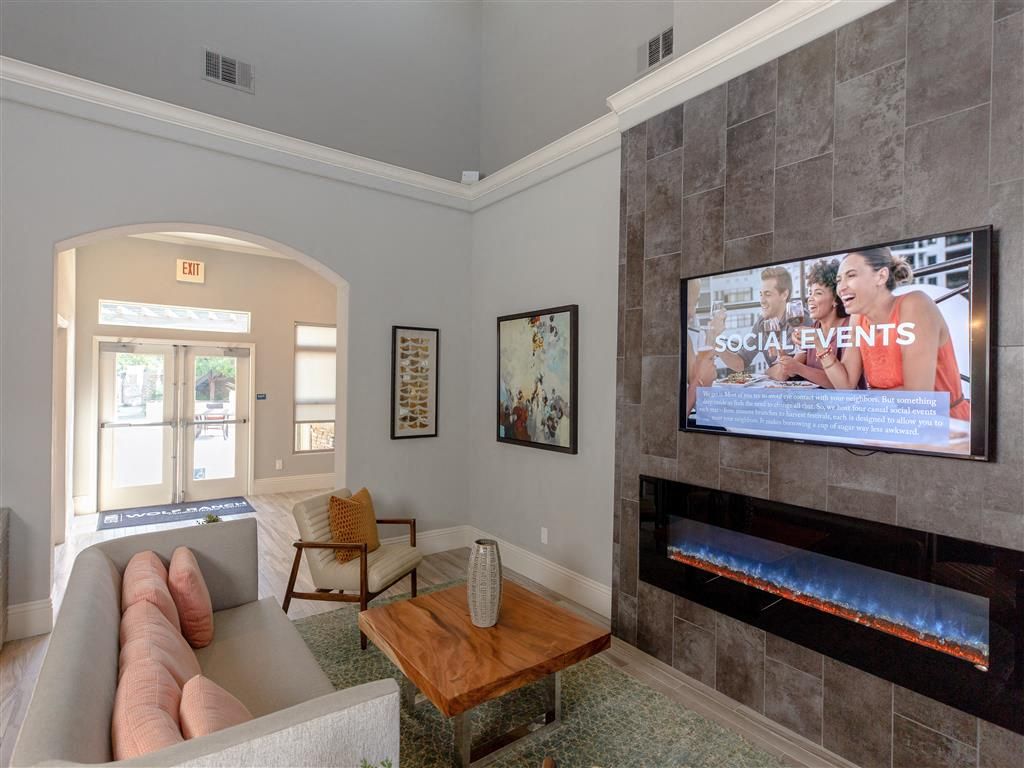 Indoor resident lounge with sofa, chair, coffee table, fireplace and wall-mounted TV at Wolf Ranch Apartments.