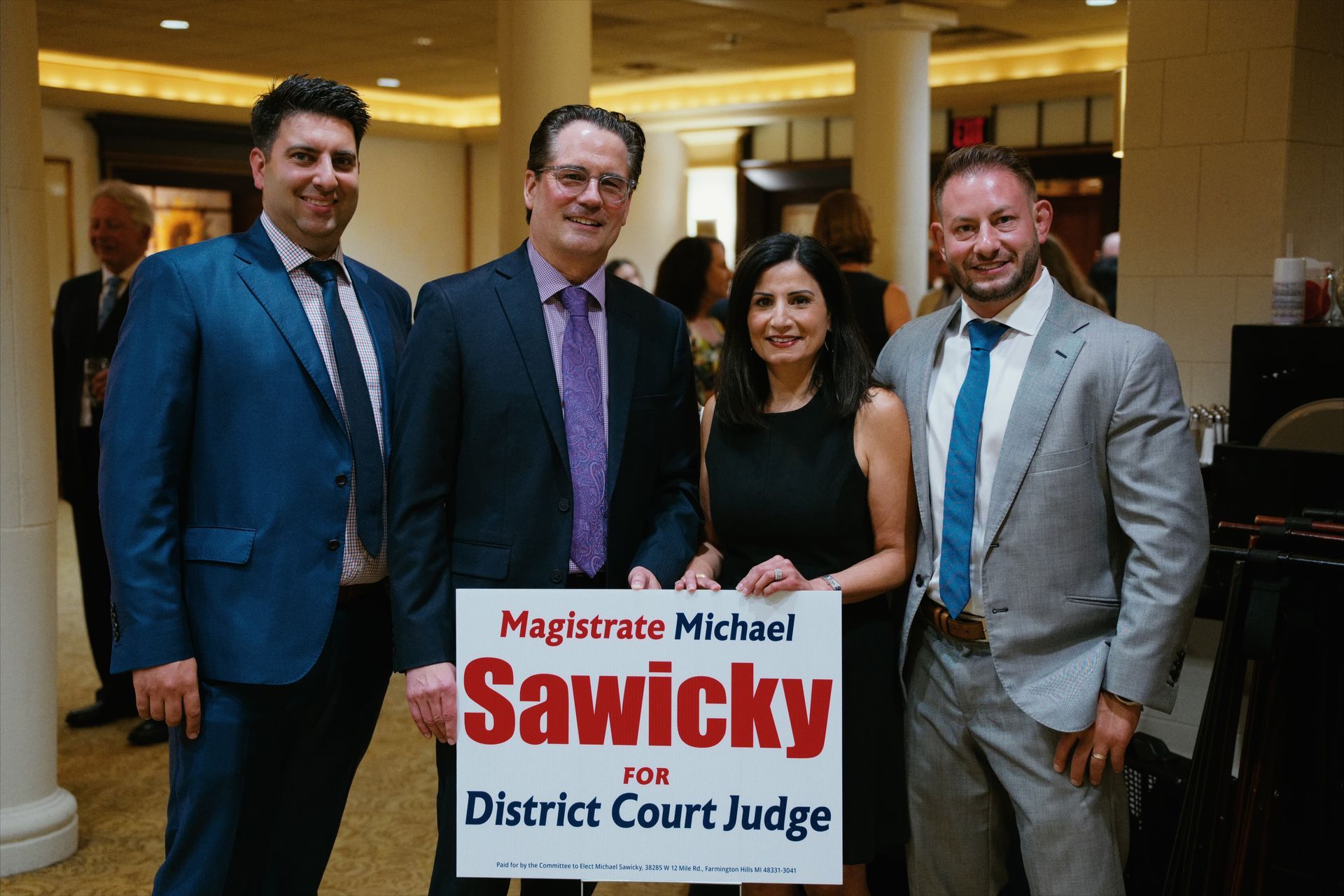 Four people pose indoors holding a sign for Magistrate Michael Sawicky, District Court Judge.
