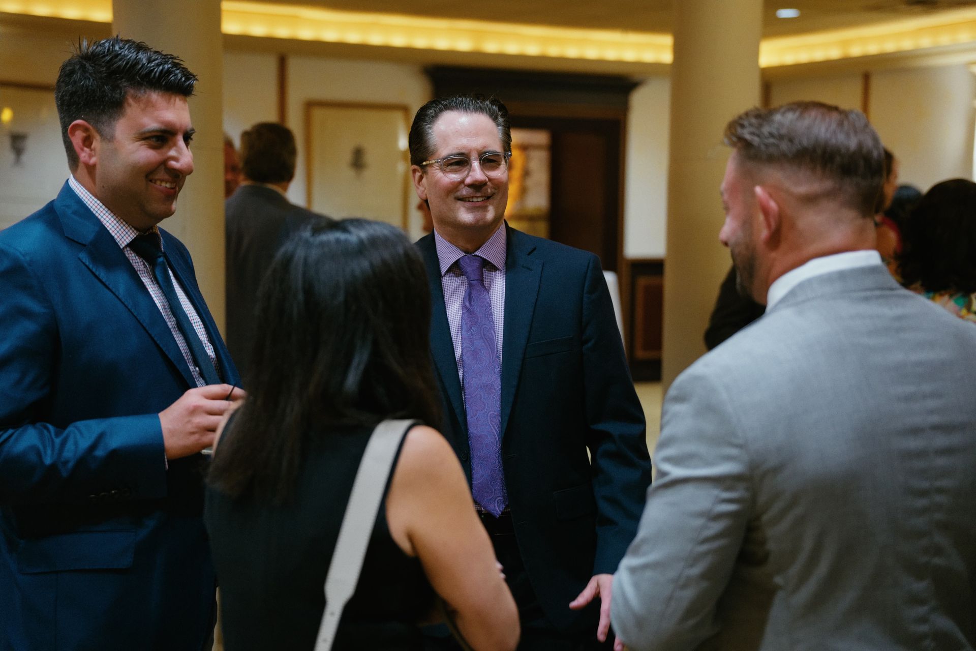 Four people in business attire talk and smile in a hotel lobby.
