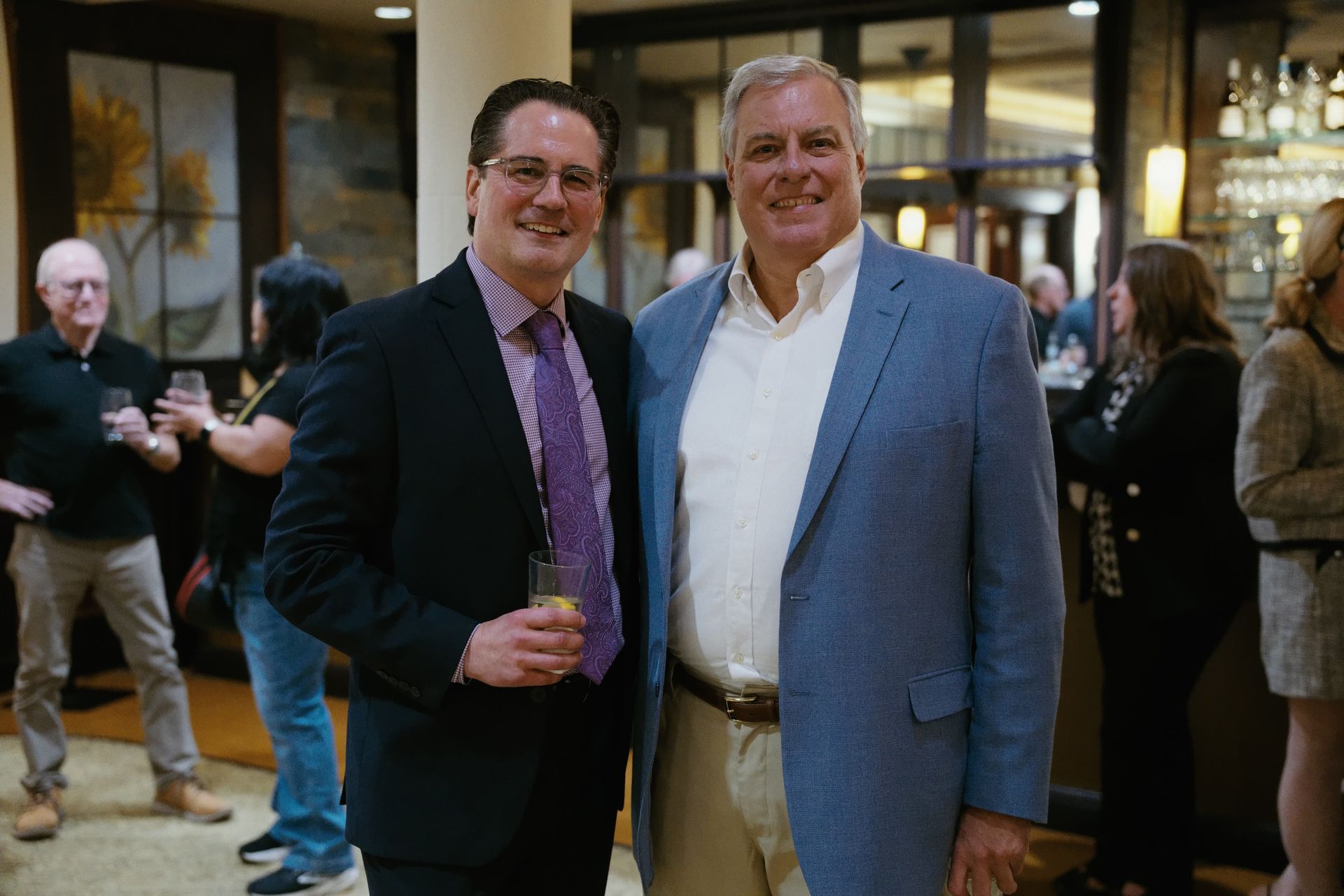Two men in suits smiling and posing at an indoor event reception