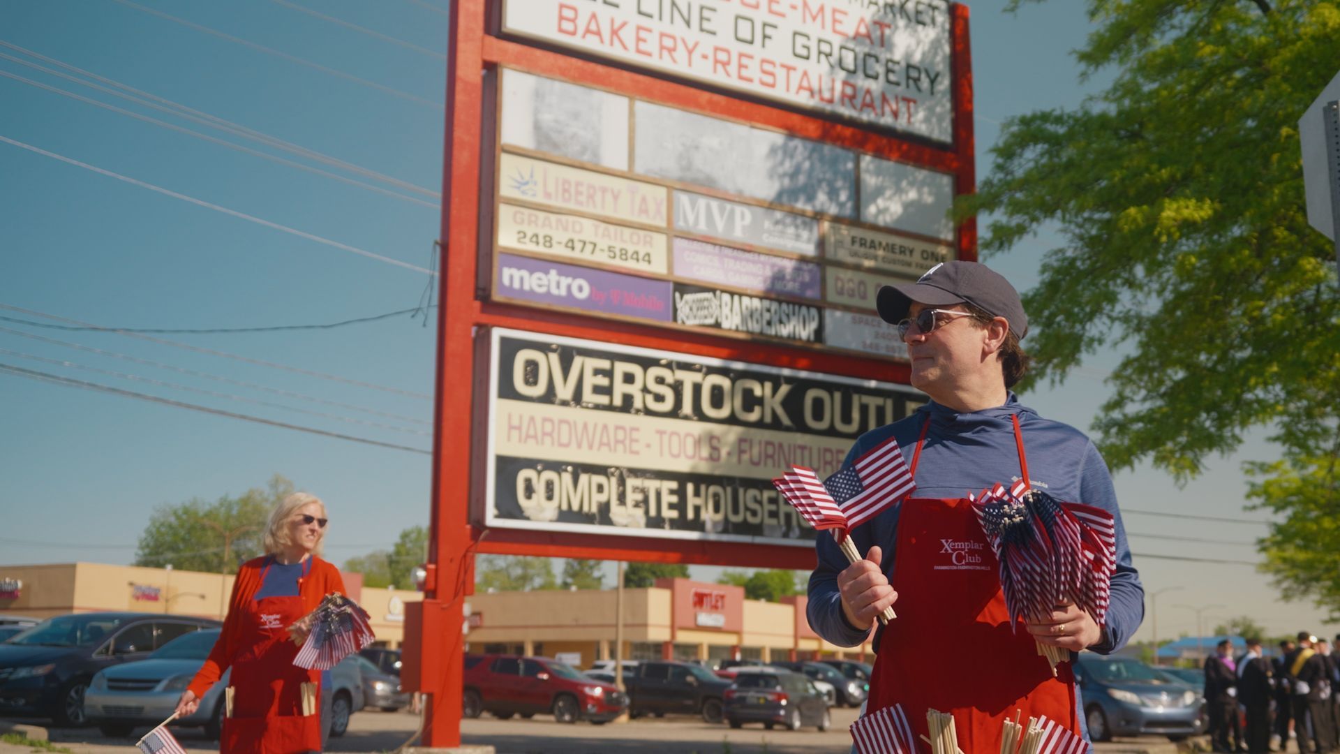 Michael Sawicky in the memorial day parade in Farmington Hills. beside a large roadside sign on a sunny street.
