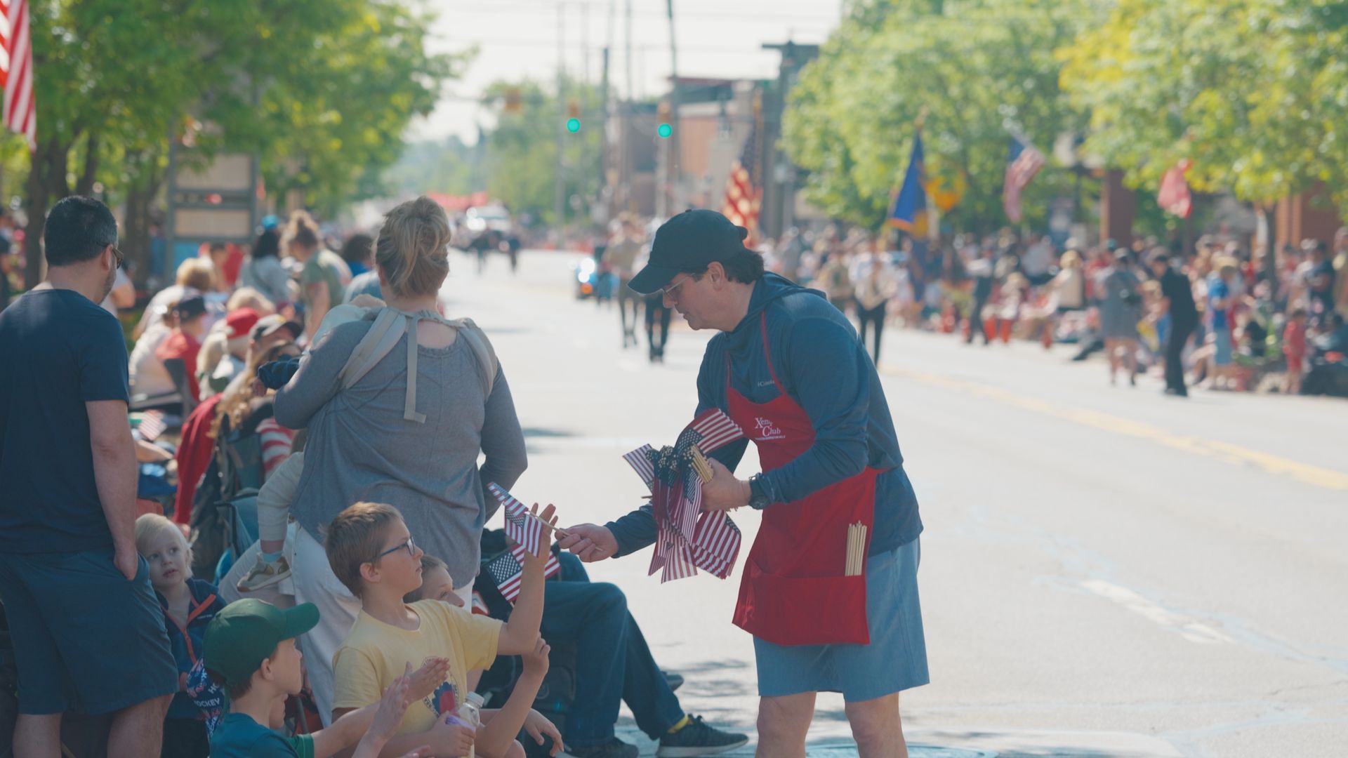 Michael Sawicky handing a drink to seated spectators along a sunny street parade route