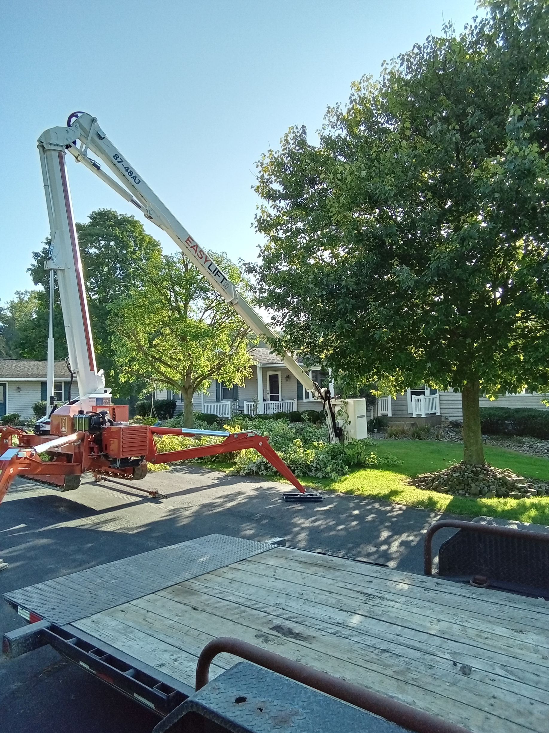 A crane is cutting a tree in front of a house.