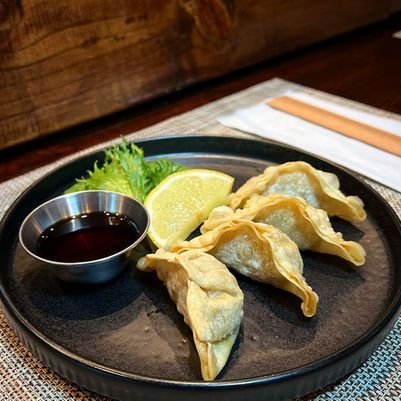 Plate of pan-fried dumplings with dipping sauce, lemon wedge, and garnish on a dark tray on a wooden table