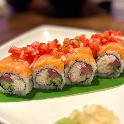 Sushi rolls topped with diced tomato and salmon on a green leaf-lined plate
