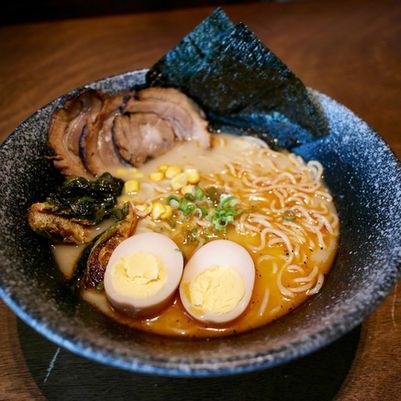 Bowl of ramen with sliced pork, seaweed, corn, green onions, and two halved soft-boiled eggs