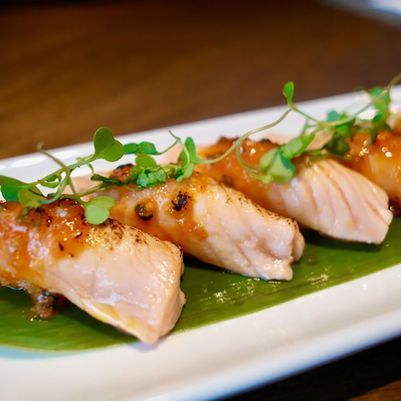 Sliced glazed fish on a banana leaf, garnished with fresh microgreens on a white plate